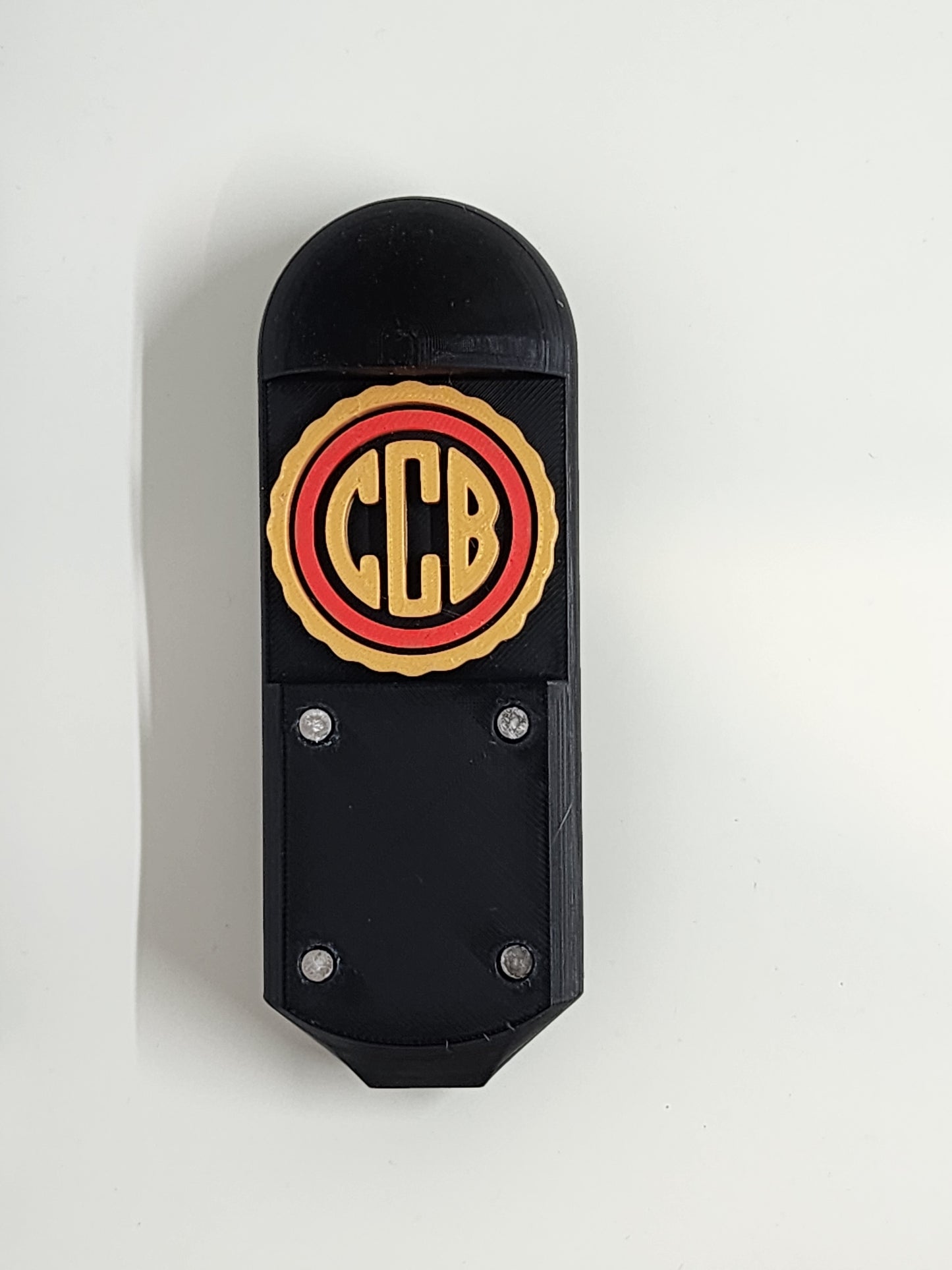 Black beer tap handle. It has the letters C C B in gold colour with a red ring around them. Around the red ring is a gold ring. Below the rings are 4 magnets inserted into the plastic. There is very minor discolouration around the magnets due to glue hazing. Glue hazing is a reaction between the plastic and the glue.